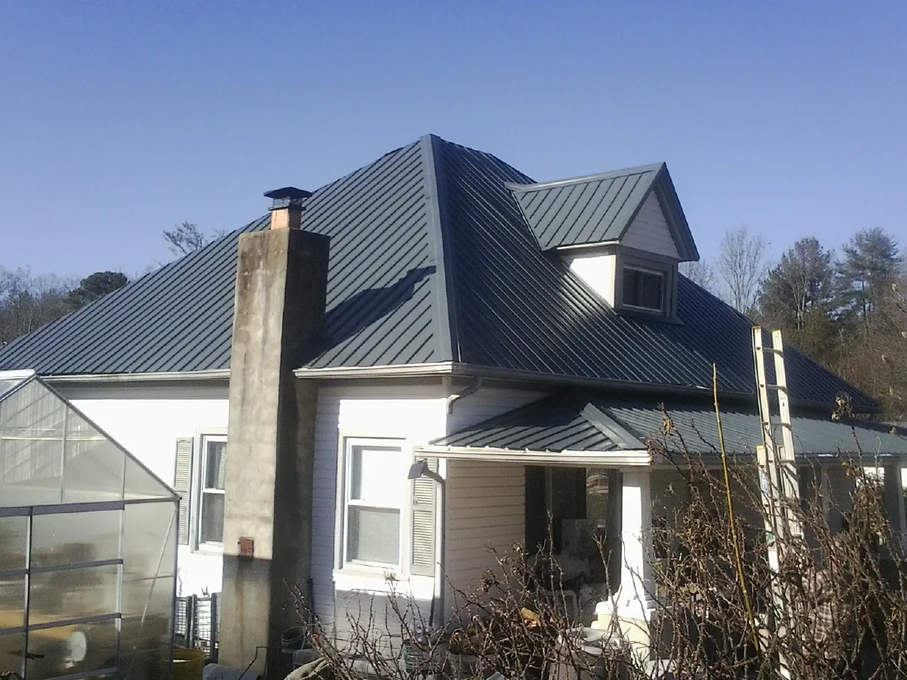 Dark blue standing seam metal roof on a white farmhouse with dormer — Slate & Tile Roof Repair by Roofing Brothers in Lascassas