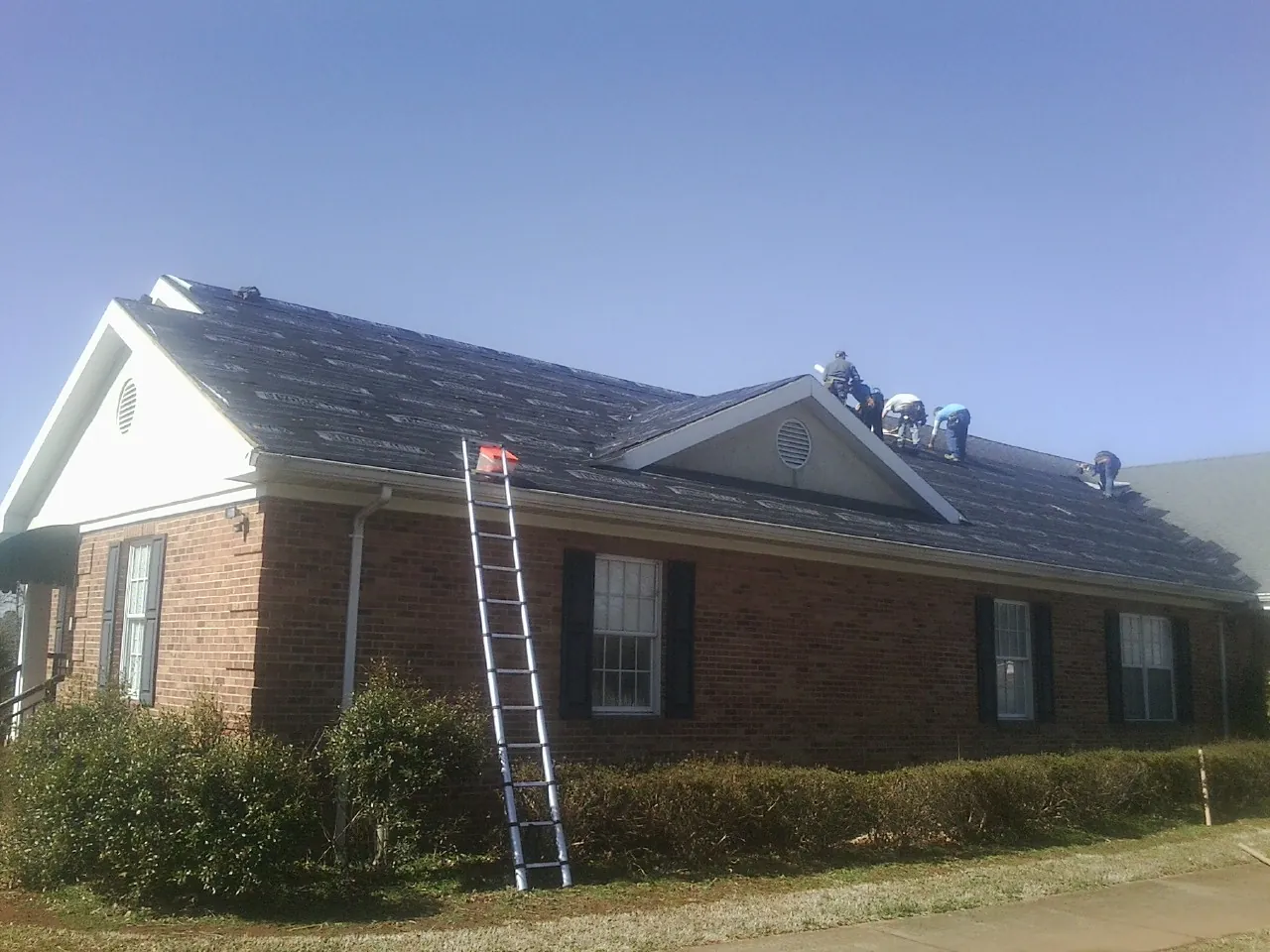 Crew tearing shingles off a brick ranch roof with a ladder set — Metal Roof Repair work by our crew in Lascassas