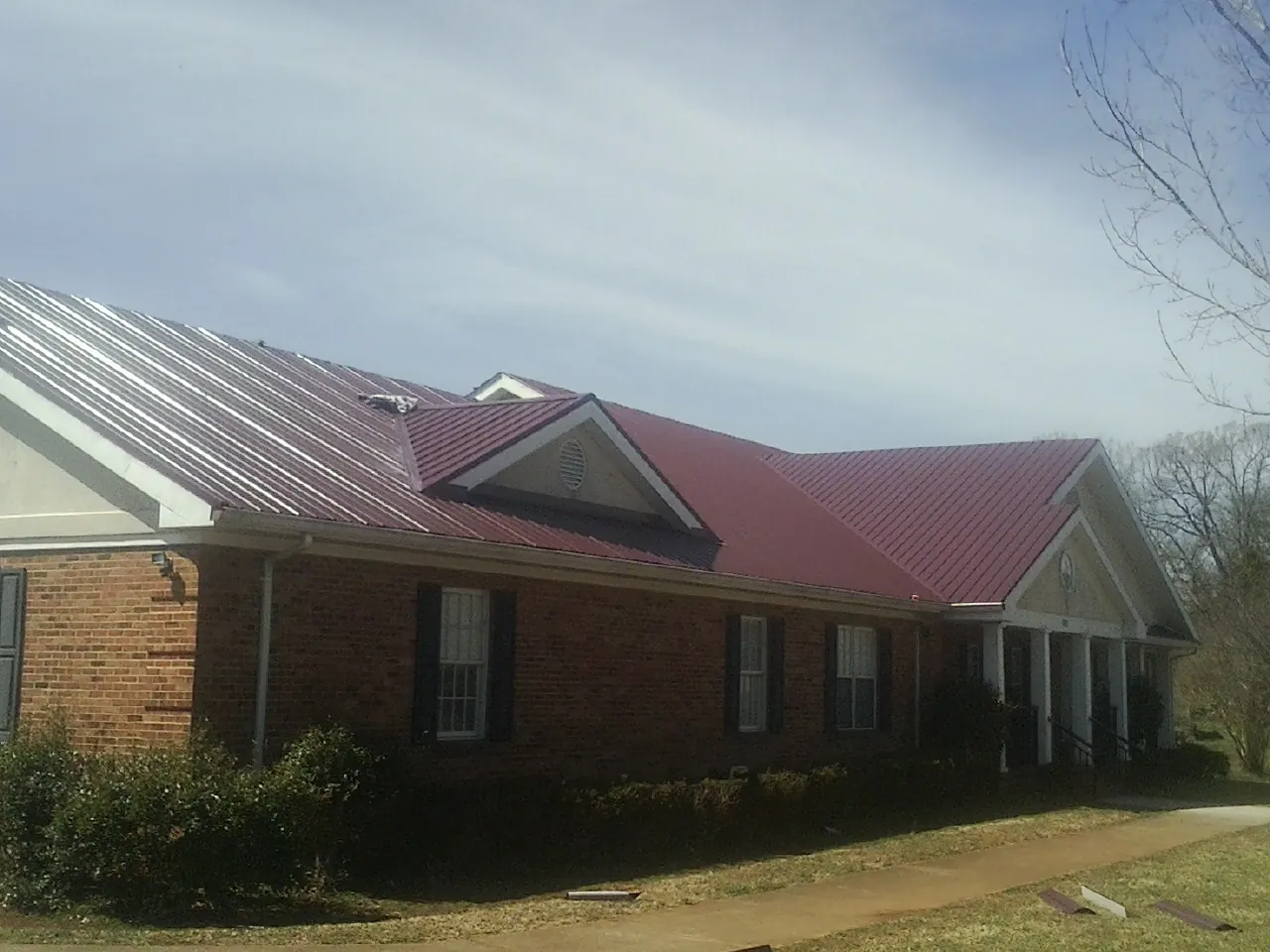 Red metal roof with gabled entries on a long brick building, from a Hail Damage Roof Repair job in Lascassas