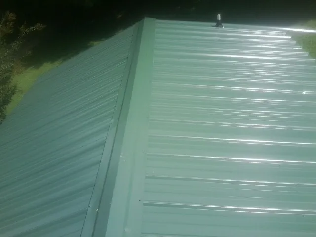 New green metal panels meeting at the ridge of a roof — Flat Roof Repair work by our crew in Lascassas