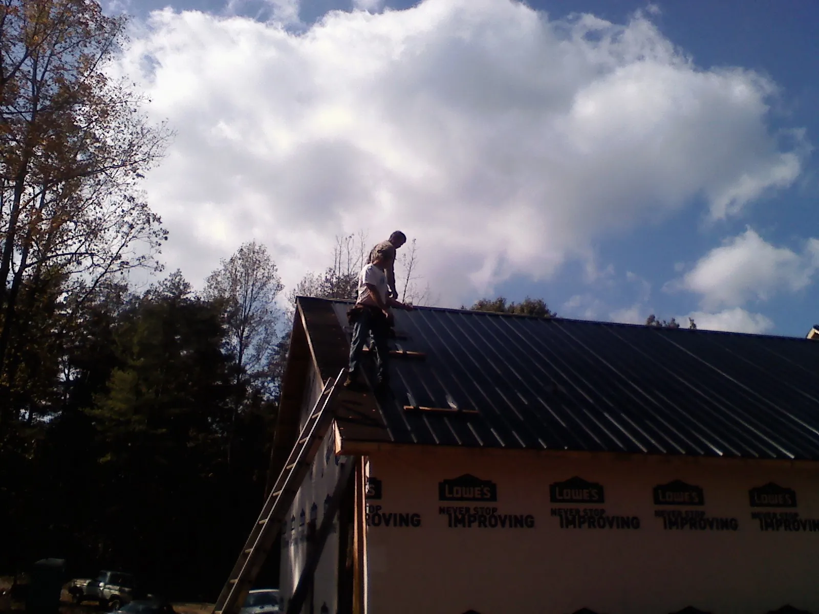 Roofer fastening dark metal panels high against a cloudy sky, from a Roof Inspection job in Lascassas