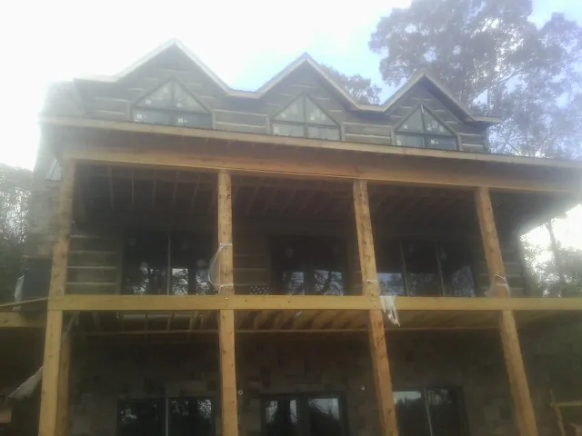 Dormers and porch framing on a large log home under construction — Roof Coating work by our crew in Lascassas