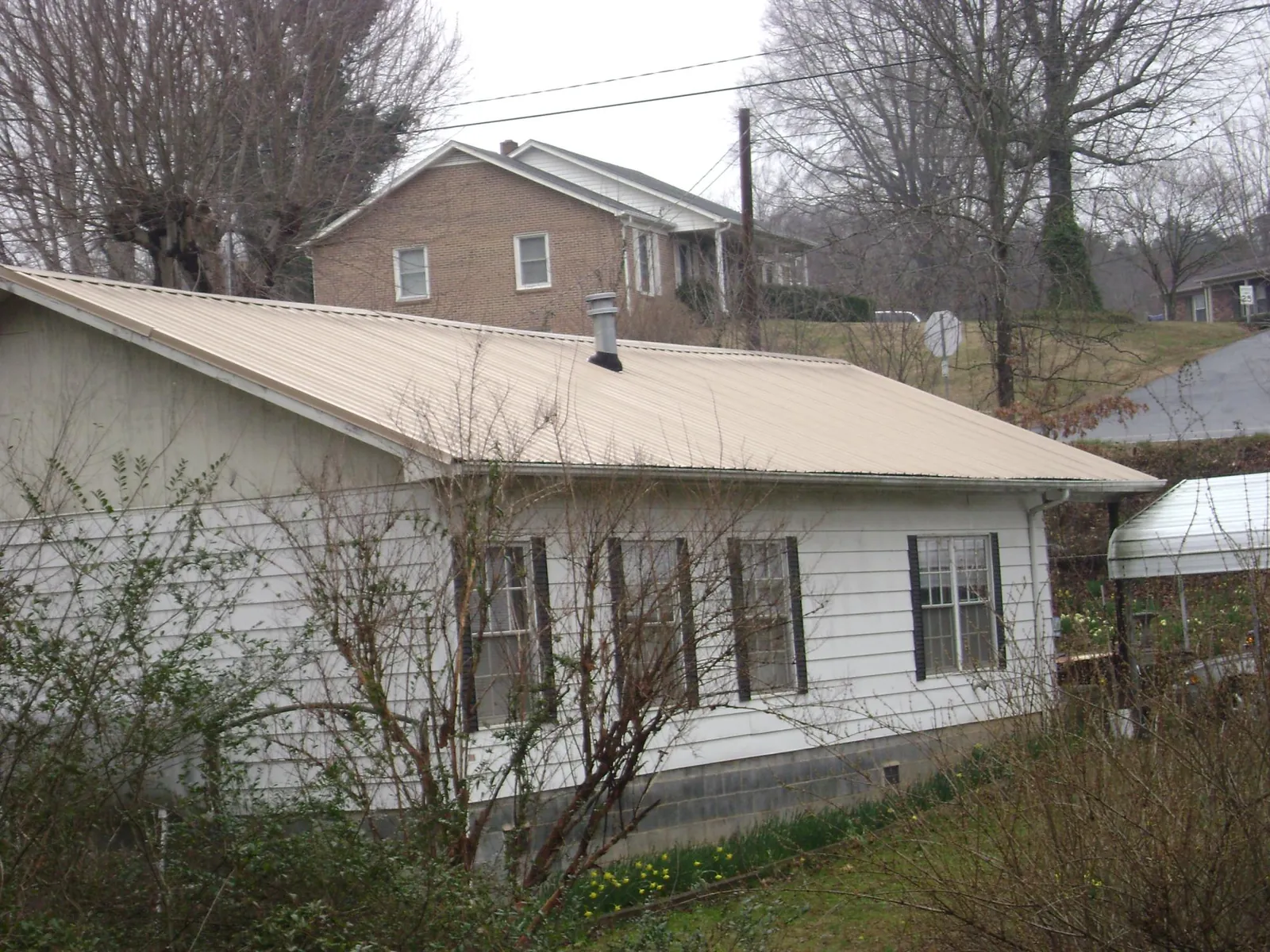 Tan metal roof on a white sided house set into a hillside — Commercial Roofing by Roofing Brothers in Lascassas