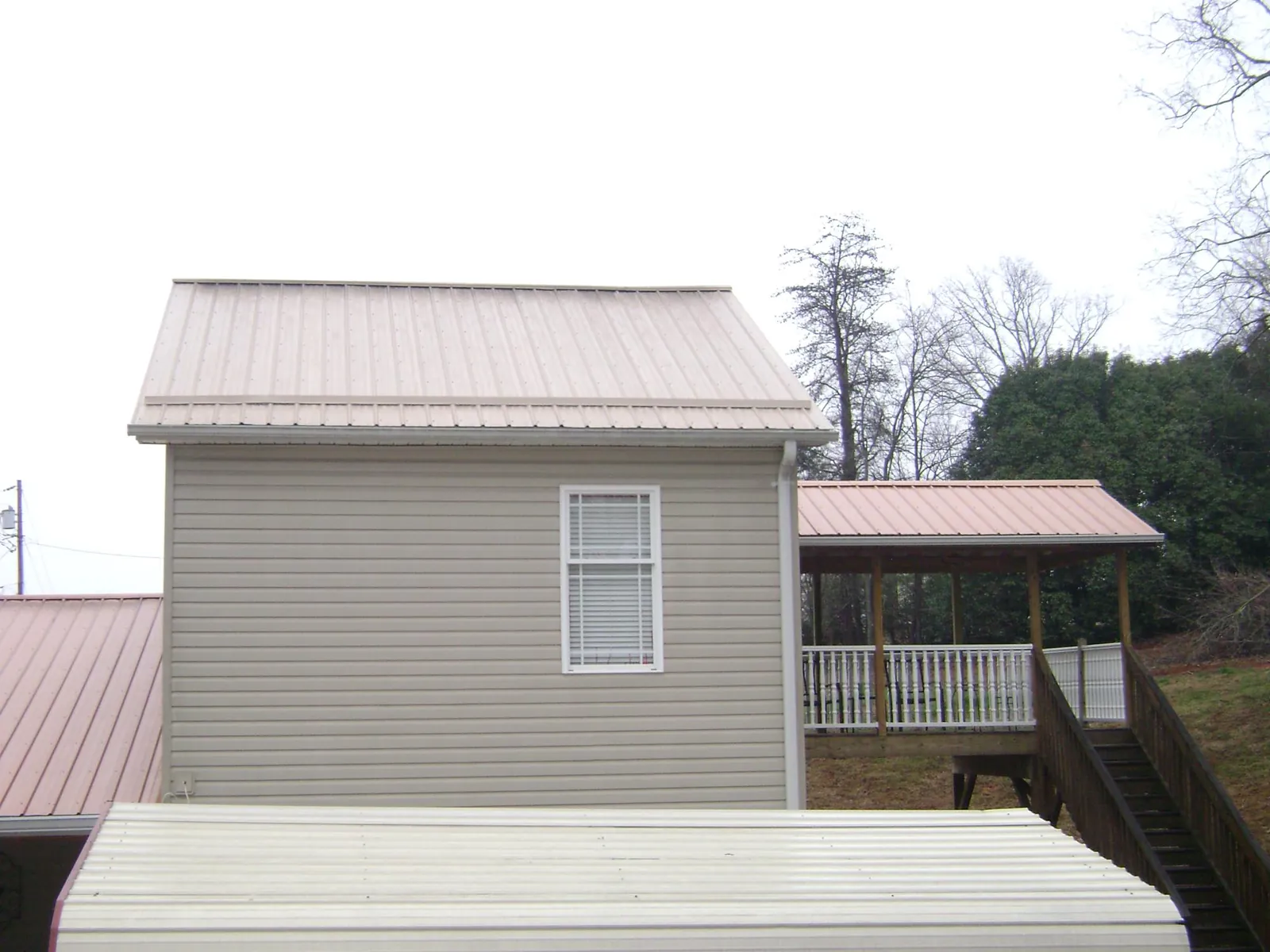 Tan metal roofs on a two story addition and attached porch, from a Roof Replacement job in Lascassas
